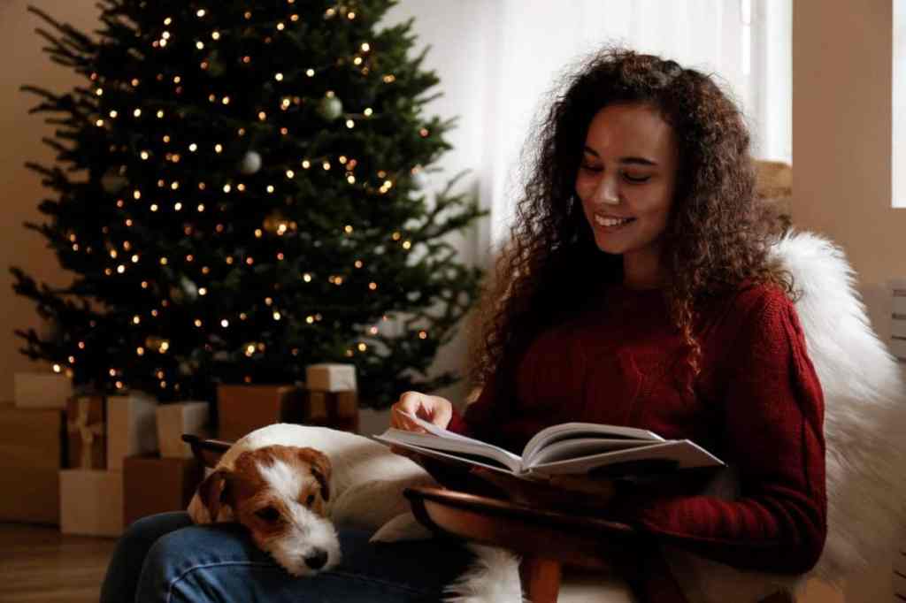 Woman sitting with dog and reading book at home.