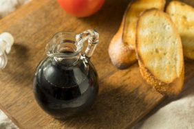 Balsamic vinegar in a glass bottle on a wooden cutting board with some bread.