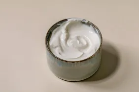 Sour cream, which dogs can eat safely in moderation, in ceramic bowl over beige background.
