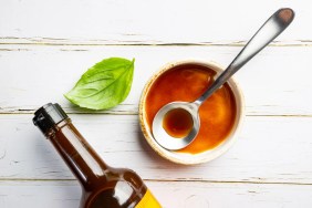 Worcestershire sauce, which dogs cannot eat, in a bowl with spoon and bottle over white background, top view