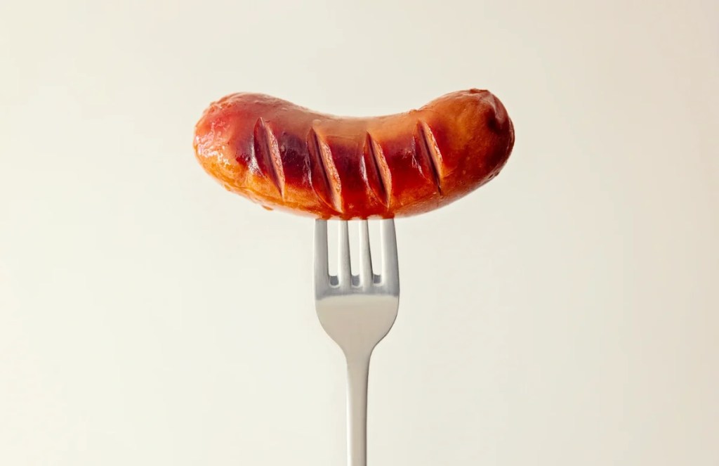 A closeup photo of cooked sausage, which dogs can eat safely if it's cooked and doesn't contain seasonings like garlic or onion, on a fork.