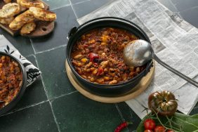 A bowl of chili with a ladle on some tile.