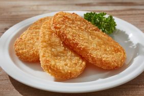 A closeup photo of a white ceramic plate, a side of parsley, and three golden hashbrowns. While dogs can eat hashbrowns, they really shouldn't due to their high fat content and salt.