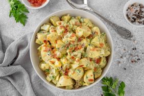 Salad of potatoes, eggs, bacon and fresh herbs with mayonnaise and yogurt dressing in a bowl on a gray concrete background