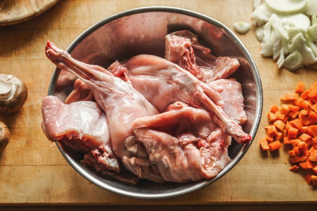 Pieces of raw rabbit meat in a bowl on kitchen table.