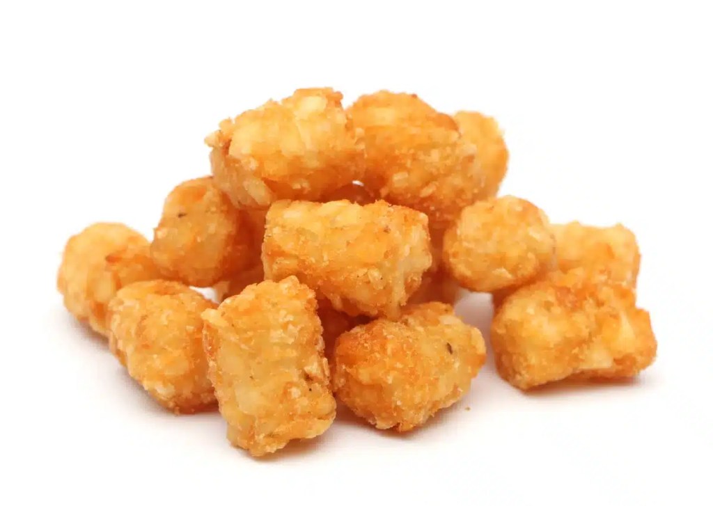 A closeup photo of a pile of tater tots against a white studio background. While dogs can eat tater tots, they really shouldn't as tater tots are not healthy dogs.